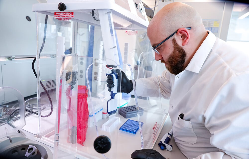 A scientist fills multiple vials at once with a manual tool inside a fume hood